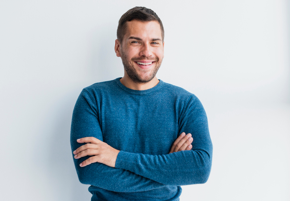 Smiling man with crossed arms wearing a blue sweater on a white background