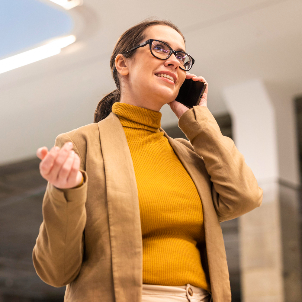 Businesswoman wearing glasses and yellow sweater talking on the phone indoors