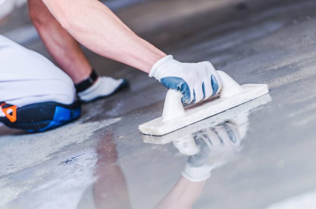 Worker smoothing wet concrete floor with a trowel during installation